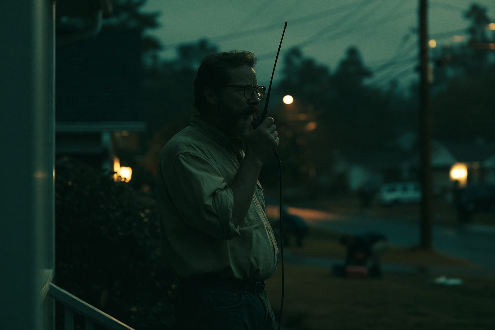 A father on his front porch at dusk, checking in on his street by handheld radio